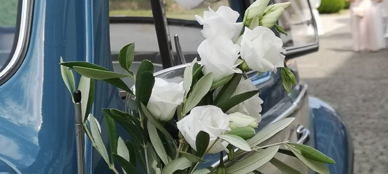 Hochzeit Hochzeitsschmuck an einem Oldtimer, im Hintergrund eine Braut