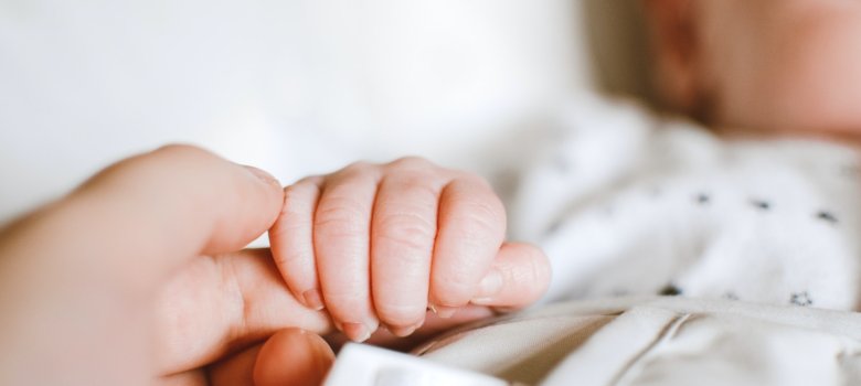 Geburt Die Hand eines Neugeborenen umschließt den Finger eines Erwachsenen