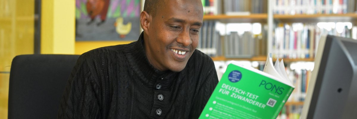 Sprachkurs Ein lächelnder Mann mit Migrationshintergrund arbeitet mit einem Sprachkurs in Buchform