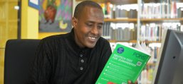 Sprachkurs Ein lächelnder Mann mit Migrationshintergrund arbeitet mit einem Sprachkurs in Buchform