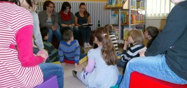 Sprach- und Leseförderung für Kinder Kinder sitzen in einem Sitzkreis zusammen und manche in der Mitte