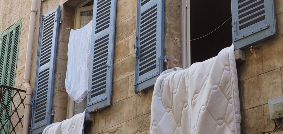 Lüften geöffnete Fenster von außen, aus denen Bettdecken und Kleider hängen um zu lüften